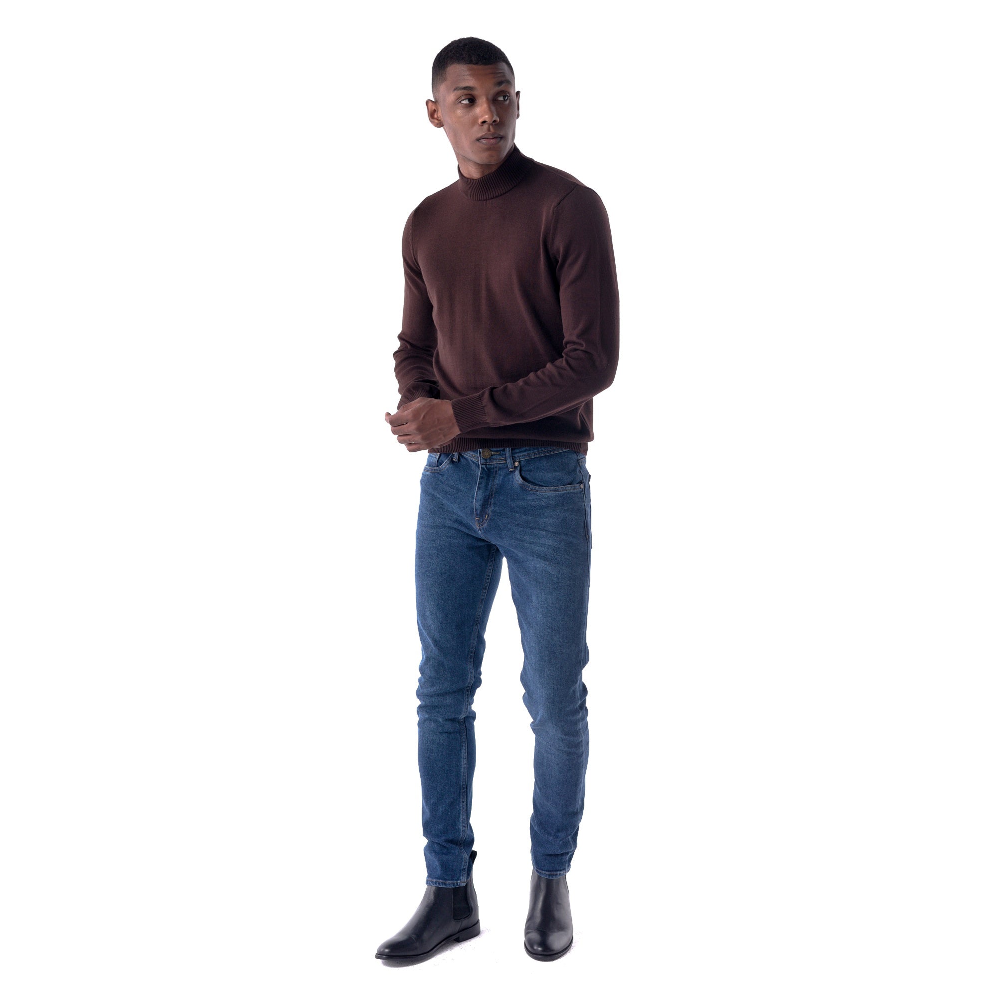 Man wearing a brown turtleneck sweater and blue jeans on a white background