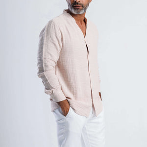 Man wearing a collarless linen blend summer shirt in soft pink, styled with white trousers and a relaxed pose.