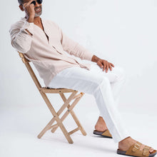 Load image into Gallery viewer, Man sitting on a chair wearing a collarless linen blend summer shirt and white pants, stylish summer outfit.
