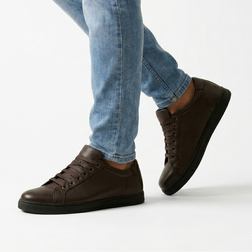 Brown leather shoes worn with light blue jeans on a white background