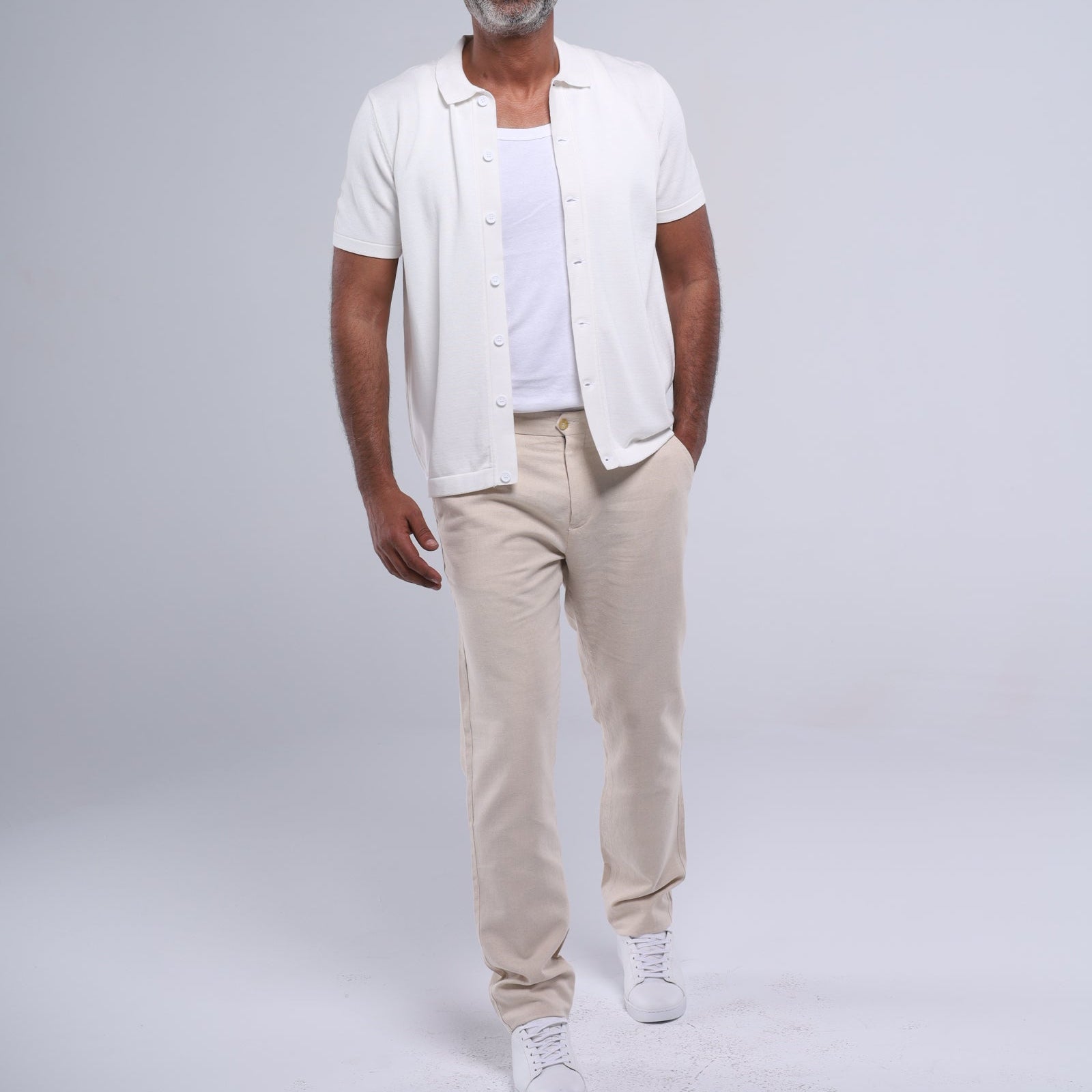Man wearing a white shirt, beige pants, and sunglasses on a gray background