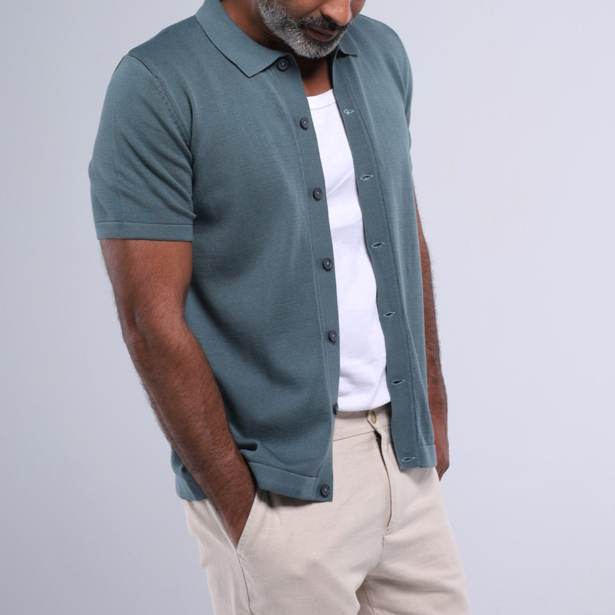 Man wearing a teal button-up shirt over a white t-shirt on a light gray background