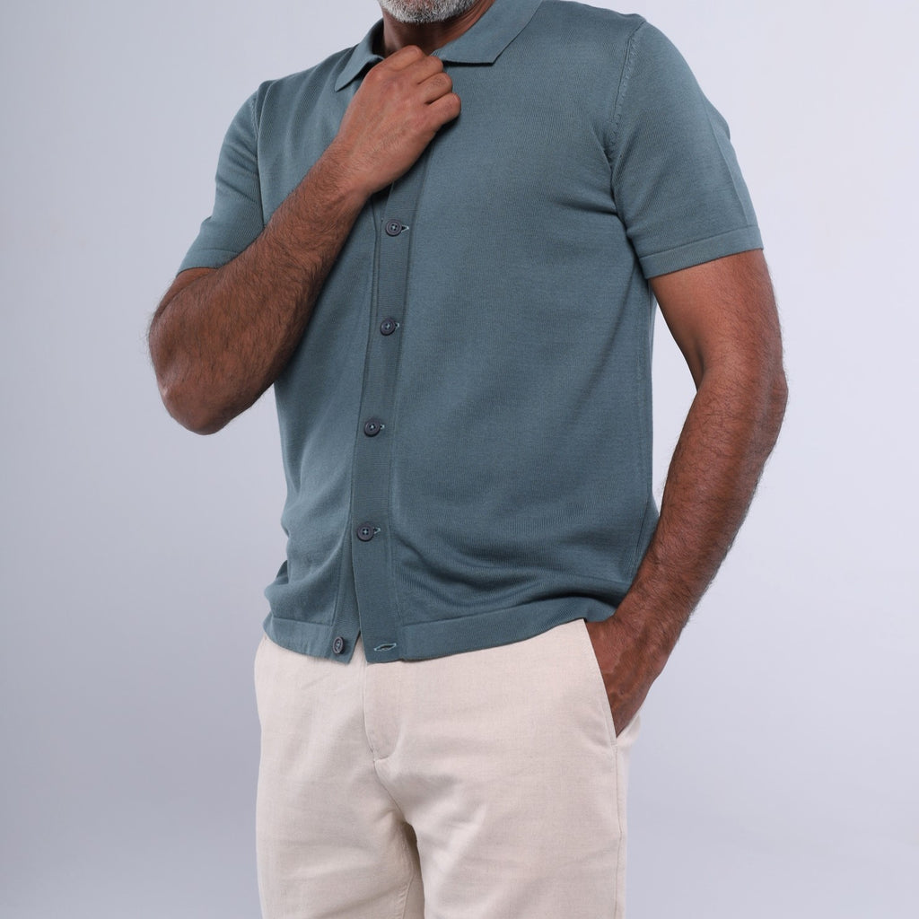 Man wearing a teal polo shirt and beige pants against a light gray background
