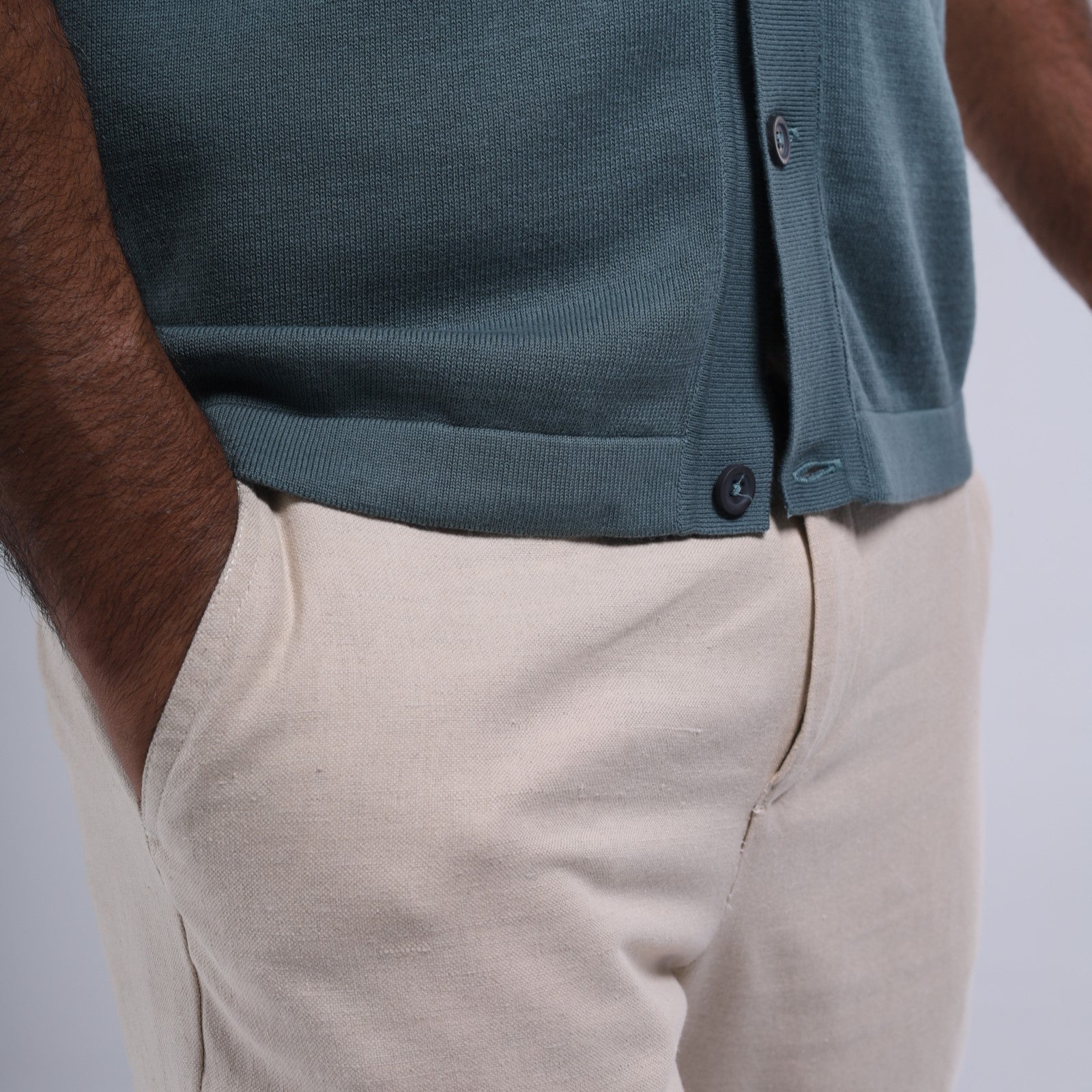 Person wearing a teal button-up shirt and beige pants on a light gray background