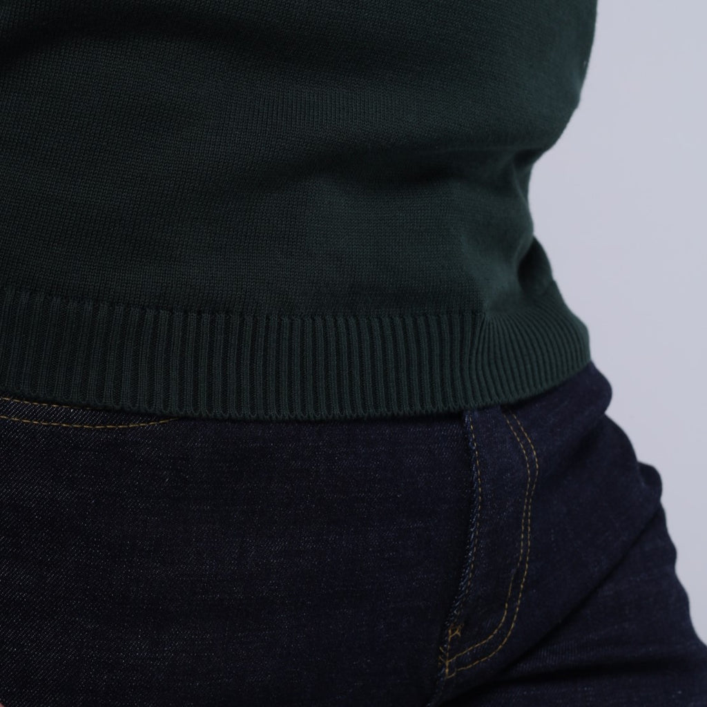 Dark green sweater and dark jeans on a light gray background