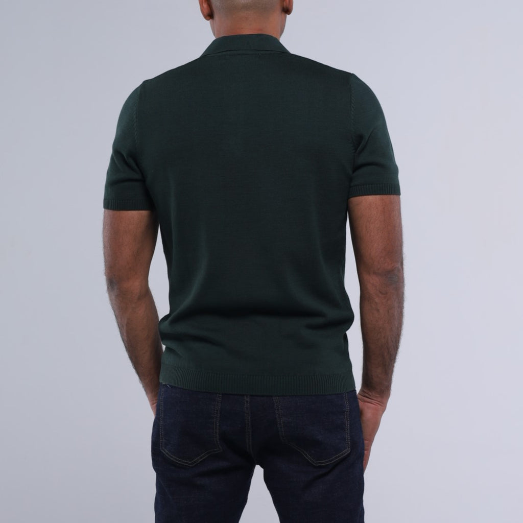 Person wearing a dark green polo shirt and dark jeans on a light gray background