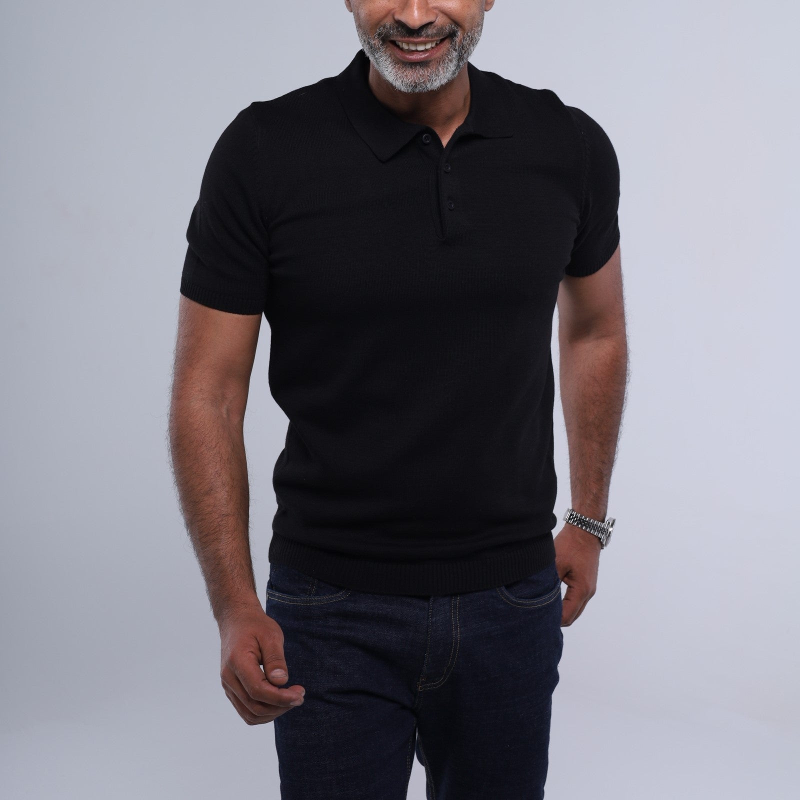 Man wearing a black polo shirt and dark jeans against a light gray background