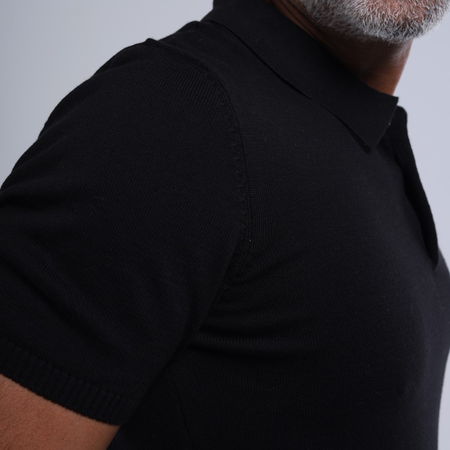 Person wearing a black polo shirt against a gray background