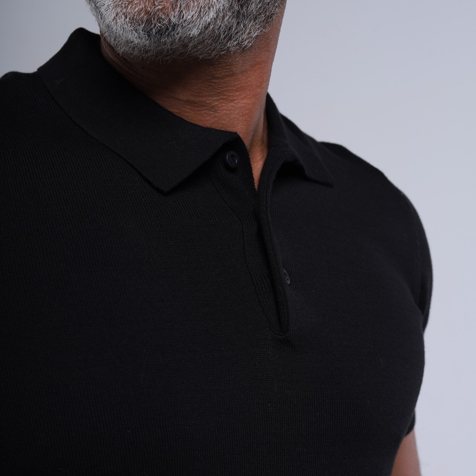 Man wearing a black polo shirt against a gray background