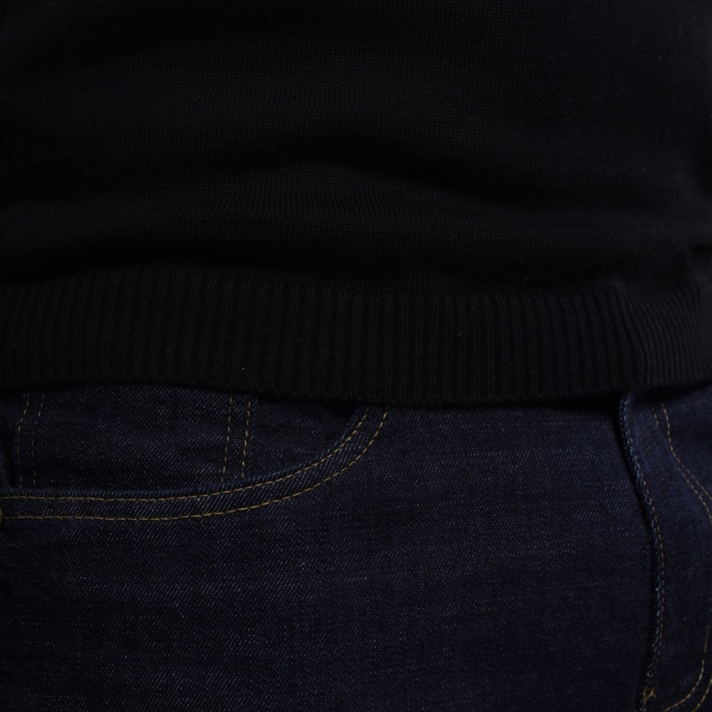 Close-up of a black sweater and dark jeans with visible stitching.