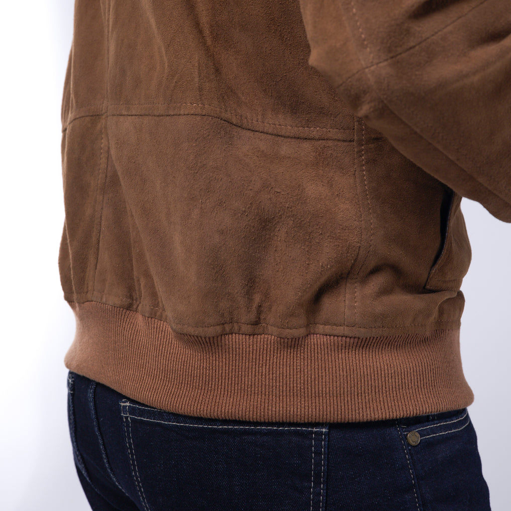 Close-up of the back waist of a brown suede jacket with a ribbed knit hem, worn by a model with dark blue jeans against a white background.
