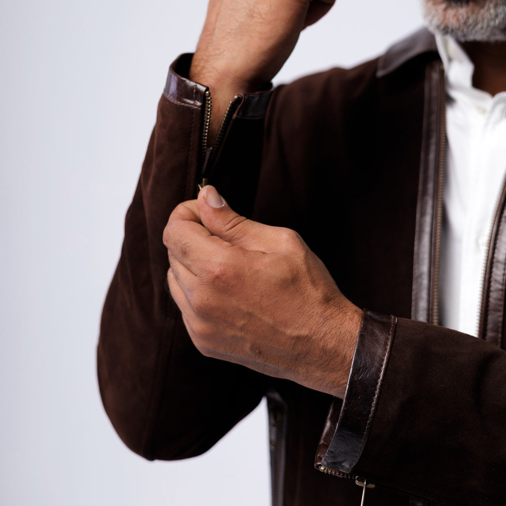 Person wearing a brown jacket with leather trim, adjusting the sleeve on a light gray background