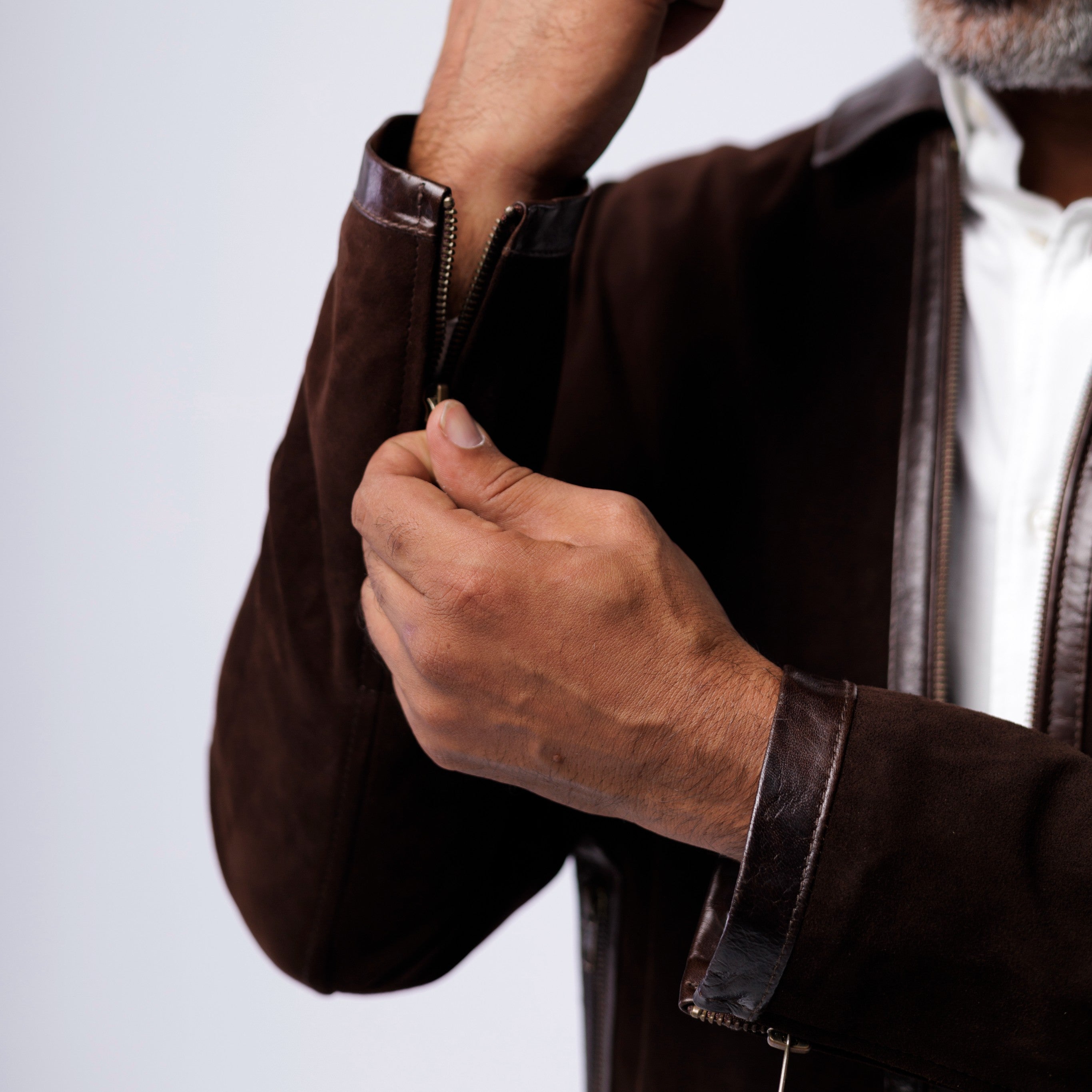 Person wearing a brown jacket with leather trim, adjusting the sleeve on a light gray background