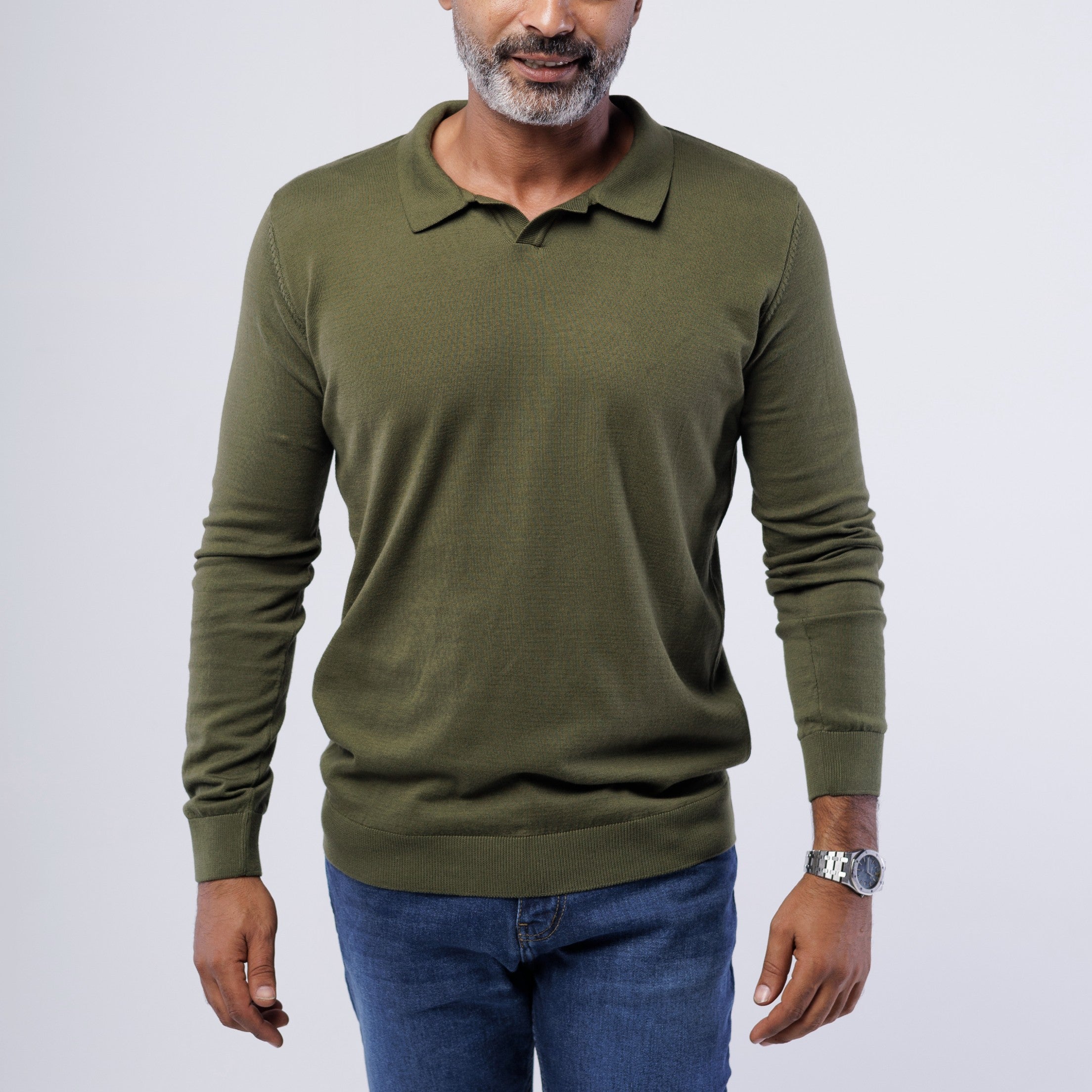 Man wearing an olive green long-sleeve polo shirt and blue jeans on a white background