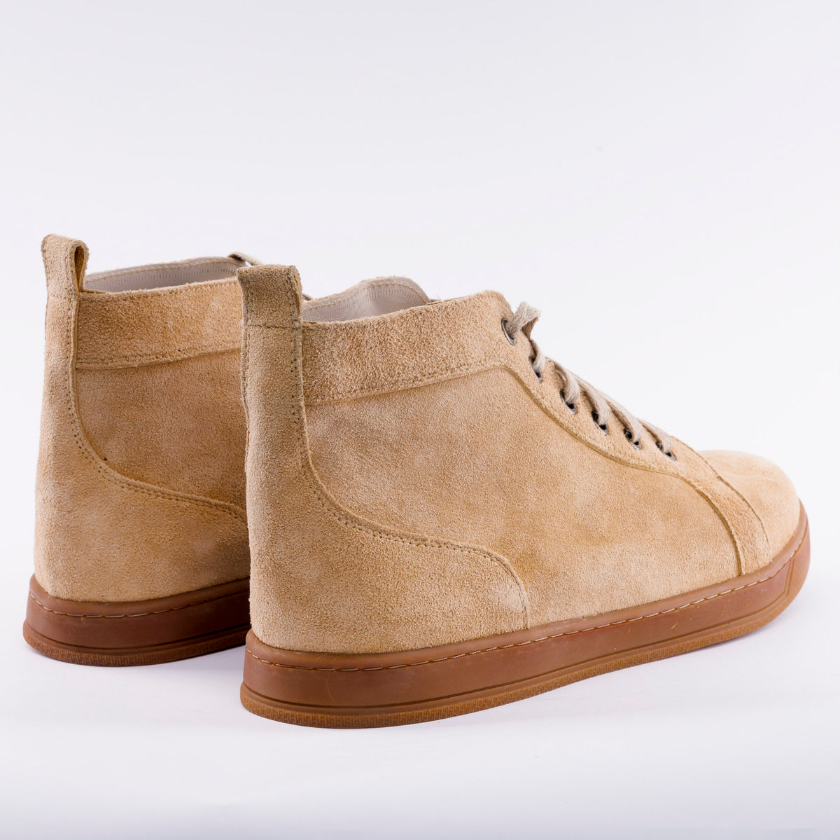 A pair of beige suede high-top sneakers with brown rubber soles, shown from a three-quarters angle on a white studio background.