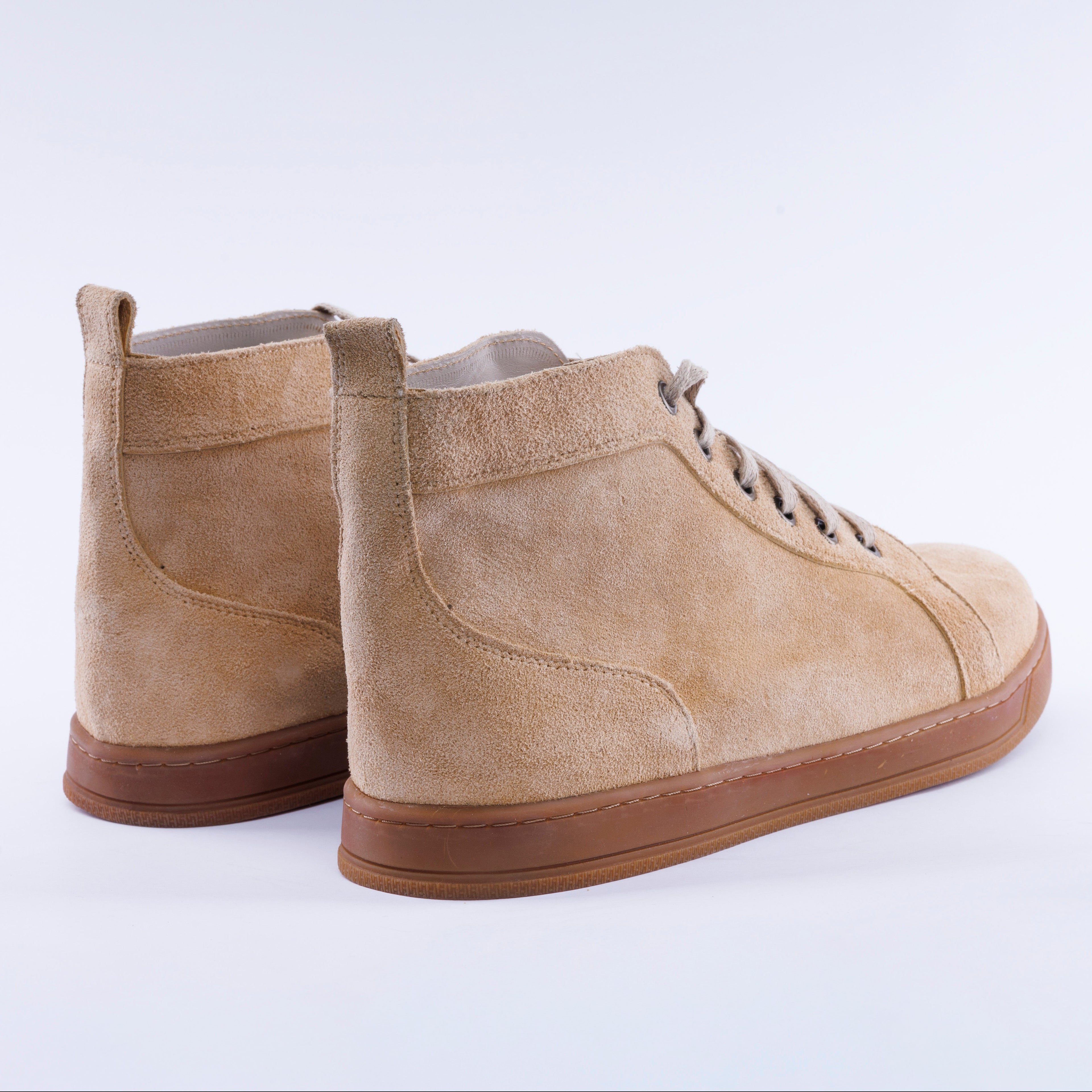A pair of beige suede ankle boots with brown soles and laces, shown from a three-quarters angle on a light gray background.