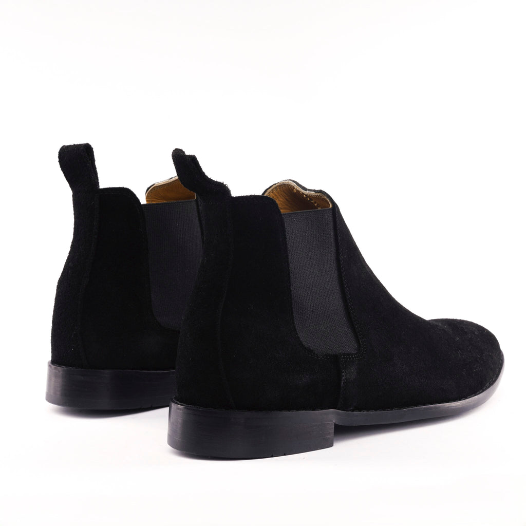 A pair of black suede Chelsea boots with black elastic side panels, shown from a rear three-quarter angle on a clean white background.