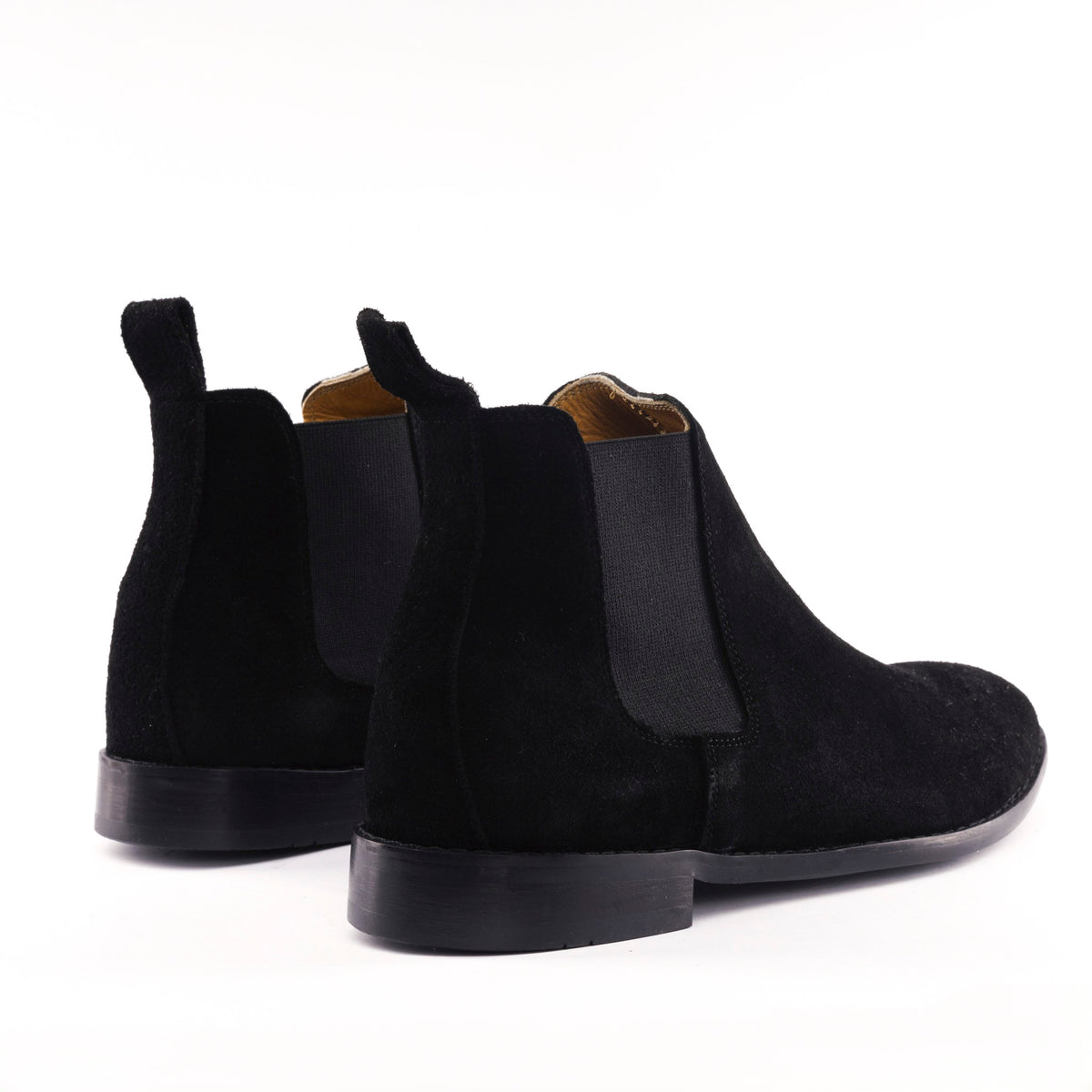 A pair of black suede Chelsea boots with black elastic side panels, shown from a rear three-quarter angle on a clean white background.