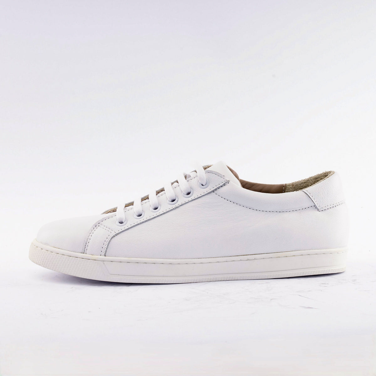 A white leather low-top sneaker with matching white laces and a white rubber sole, shown in a side profile against a clean white background.