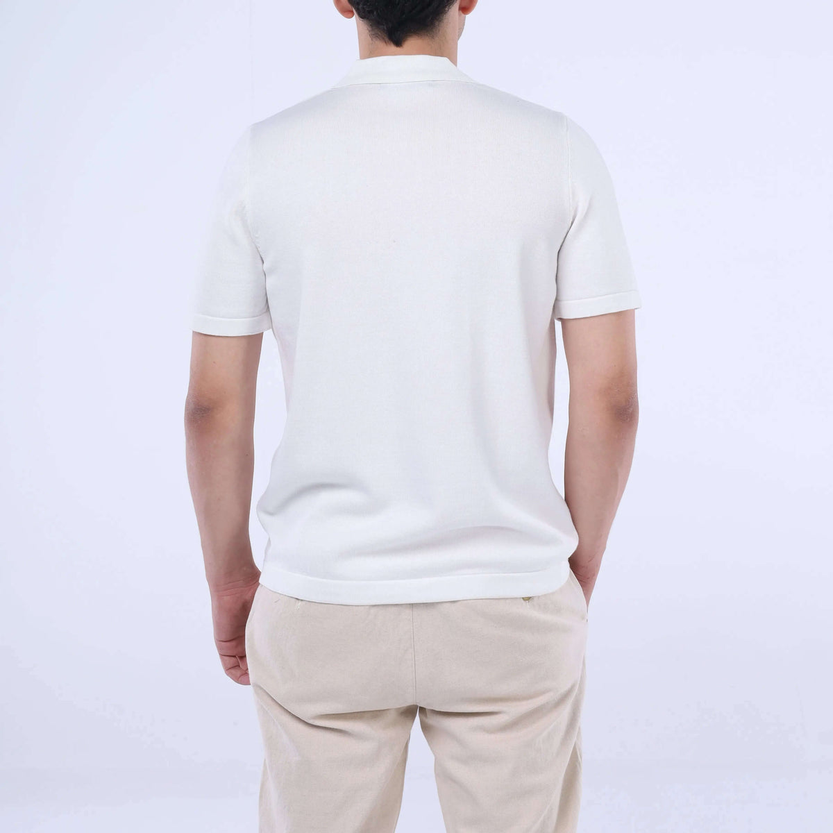Back view of a man wearing a solid Knit-Layer™ Short Sleeve Shirt in white, paired with beige pants.