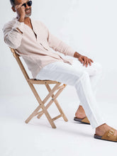 Load image into Gallery viewer, Model wearing a casual linen blend tapered trouser and stylish shirt, seated on a wooden chair with sunglasses.
