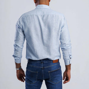 Back view of a man wearing a light blue linen blend slim fit shirt with long sleeves and casual jeans.