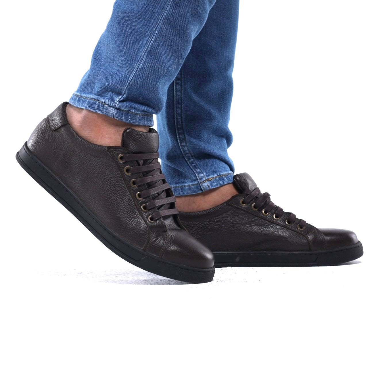 Brown leather sneakers worn with blue jeans on a white background