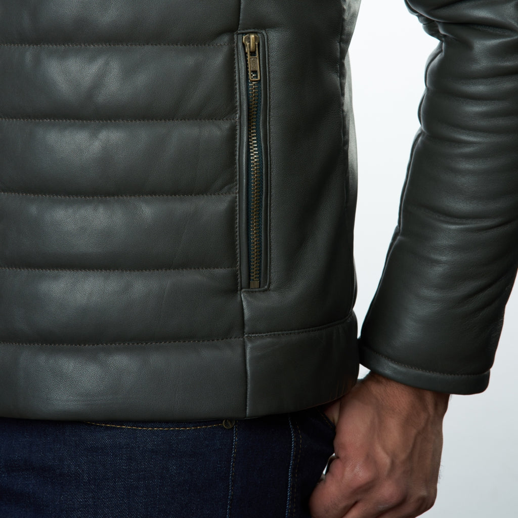 Close-up of a person wearing olive leather jacket with a zipper on a light gray background
