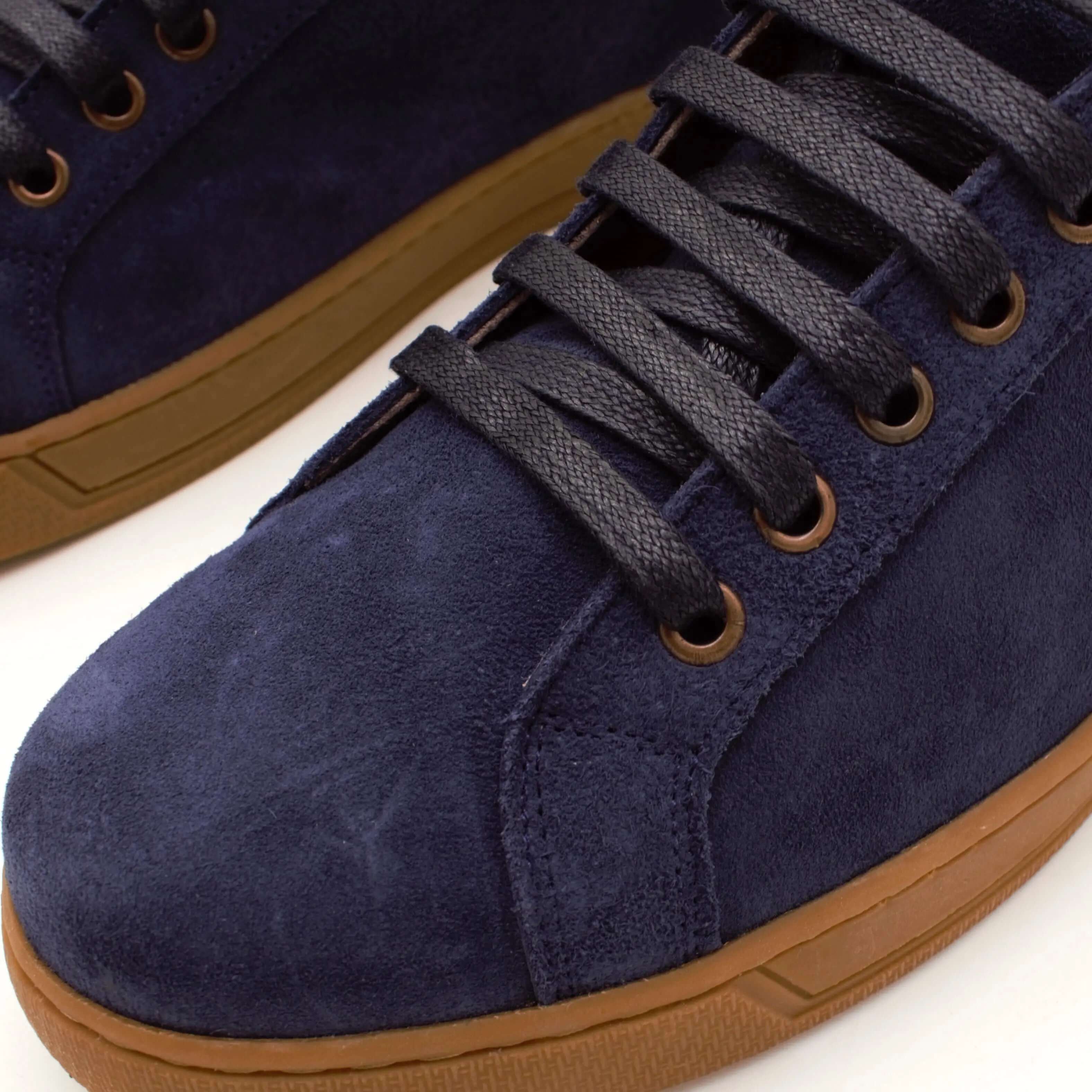 Close-up of handcrafted navy suede low-top sneakers with brown rubber sole and black laces.