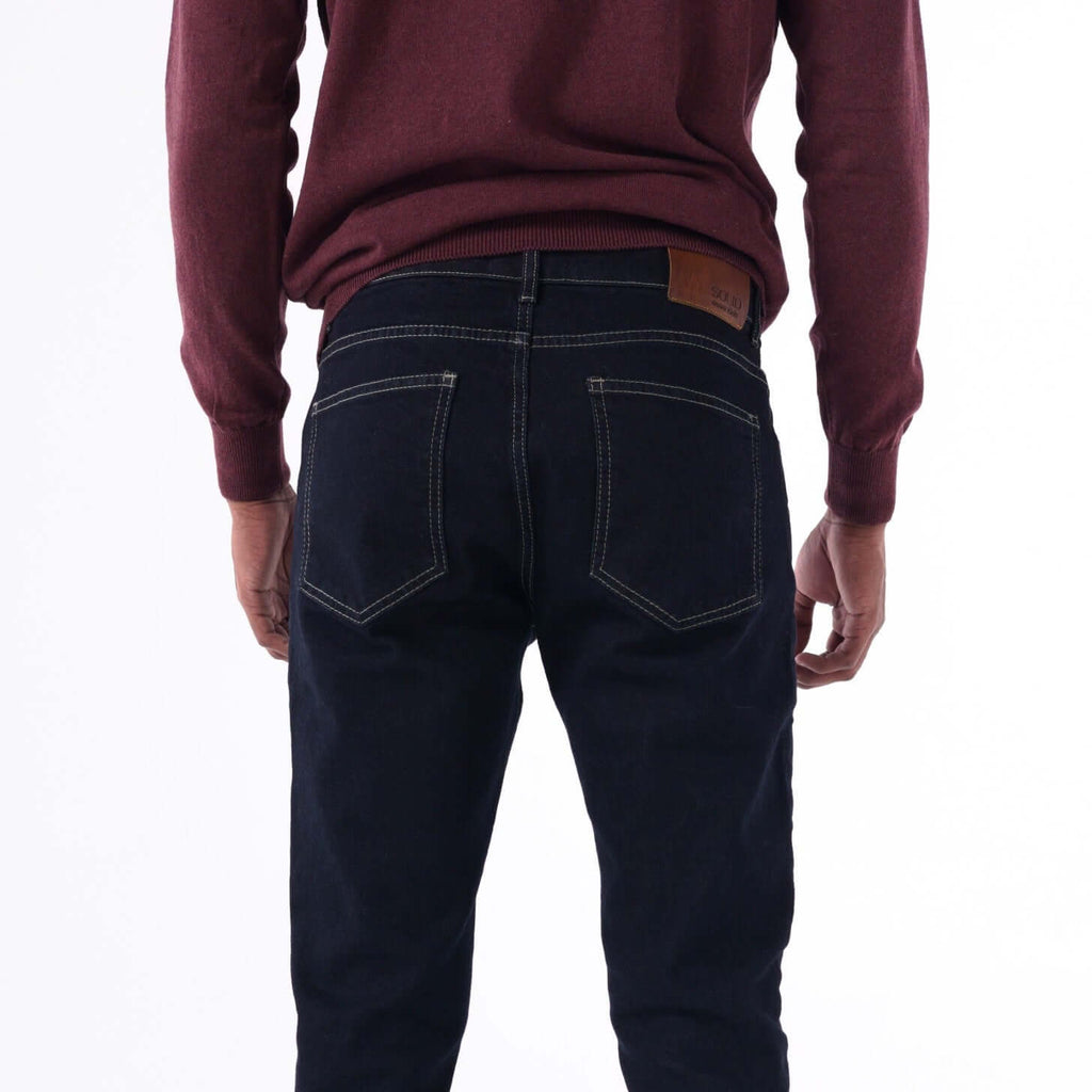 Back view of a man wearing SOLID navy slim denim jeans with beige contrast stitching.