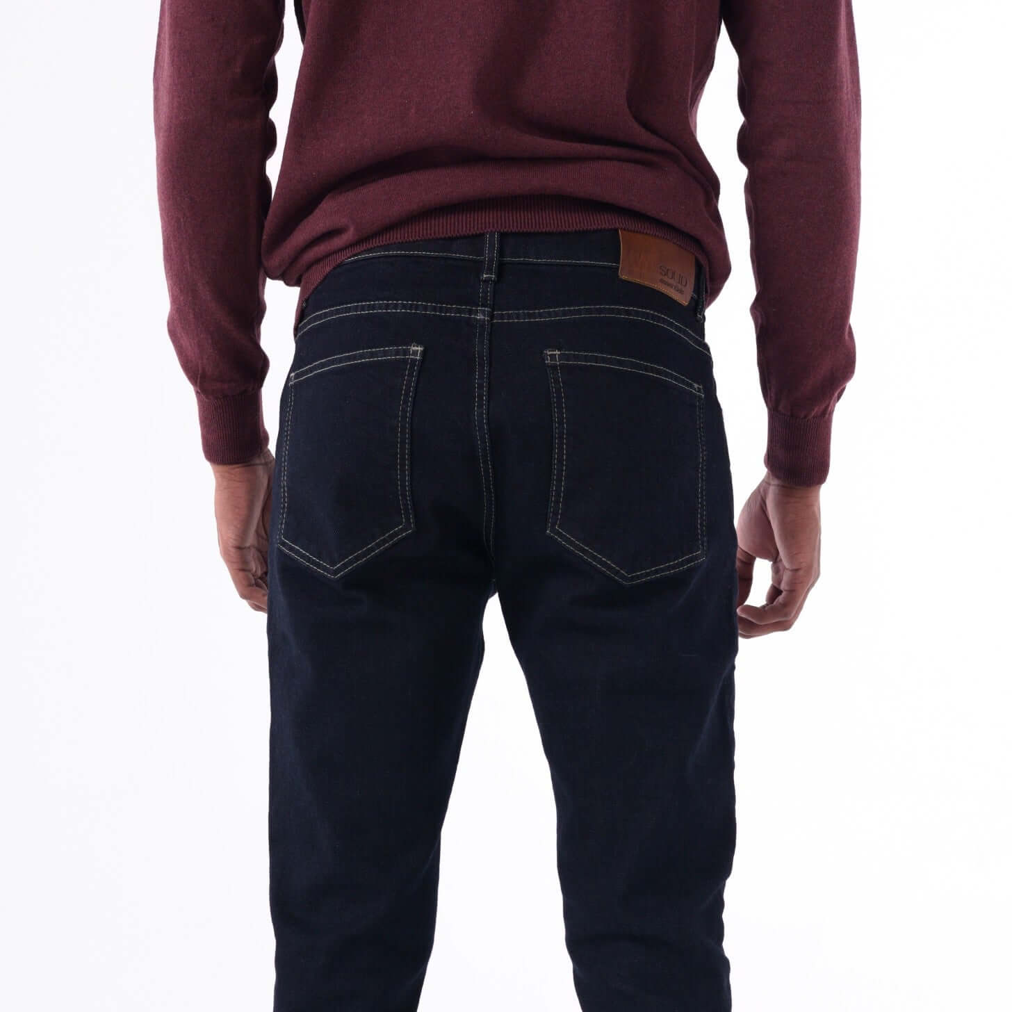 Back view of a man wearing SOLID navy slim denim jeans with beige contrast stitching.
