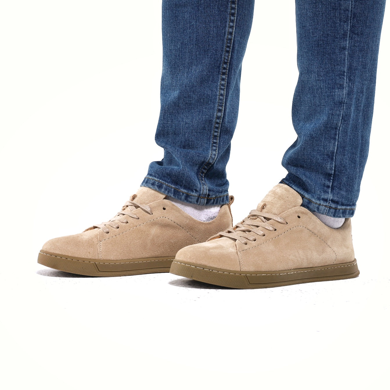 Beige sneakers worn with blue jeans on a white background