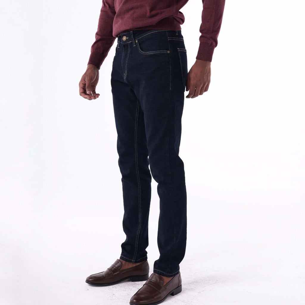 Navy slim denim jeans with contrast stitching, styled with a maroon sweater and brown shoes.