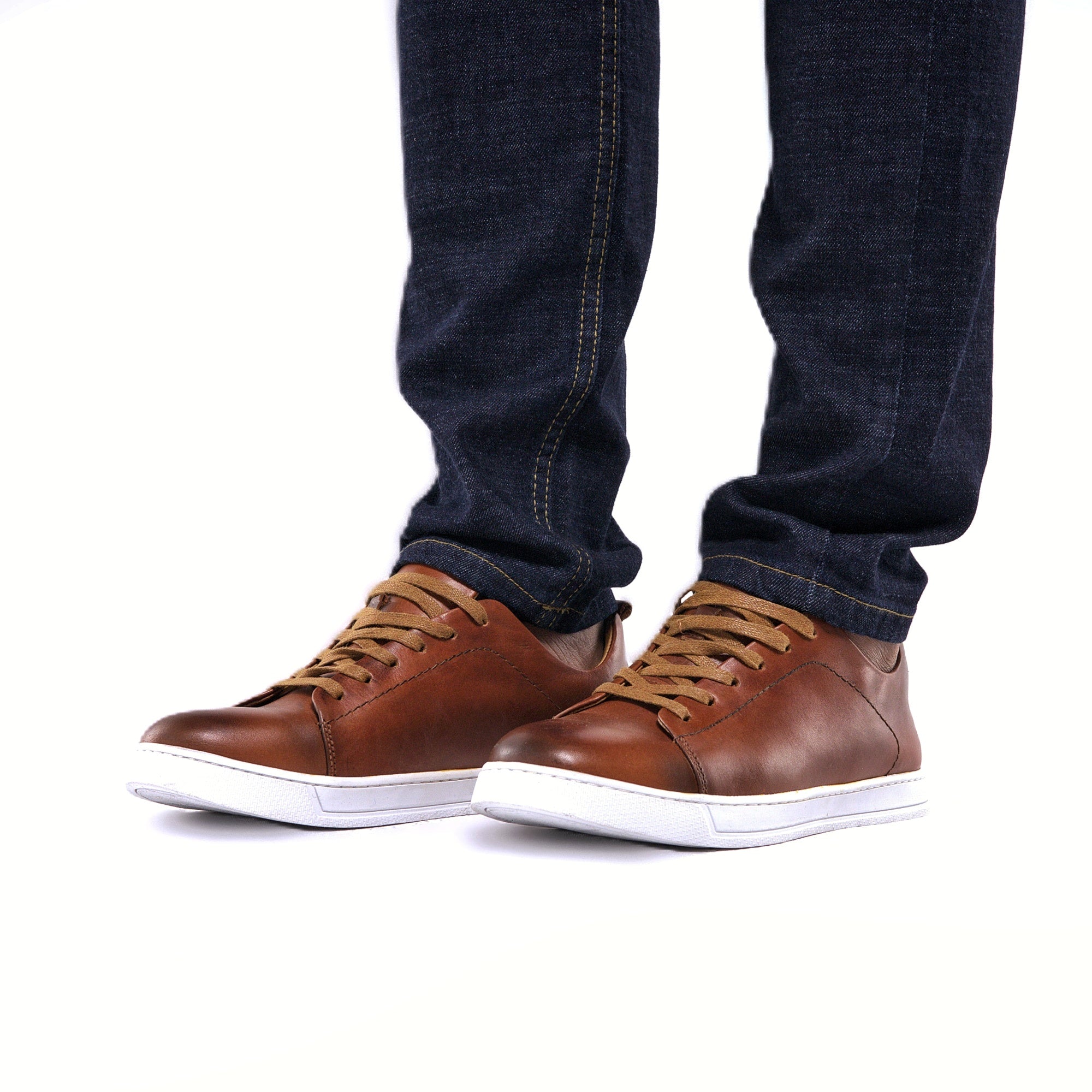 Brown leather sneakers with white soles worn with dark jeans on a white background